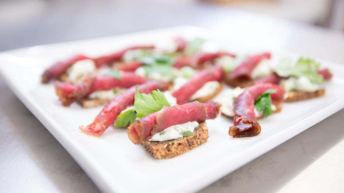 Beef carpaccio with creamy spread on toasted bread garnished with herbs.